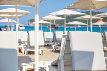 Beach chairs and umbrellas on the beach. White sun loungers with mattresses and parasols stand on the tropical beach