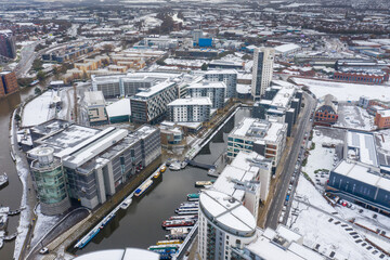 Aerial photo of a snowy winters day in the city of Leeds in the UK showing the area in Leeds known as the Leeds Dock near the Leeds and Liverpool canal and the Royal Armouries Museum covered in snow.