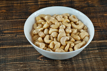 Cashews in a white bowl on an old shabby board. Nuts on a brown wooden table.