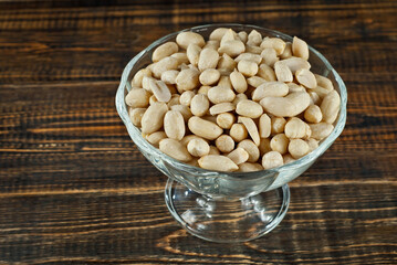Peanuts in a transparent bowl on an old shabby board. Nuts on a brown wooden table.