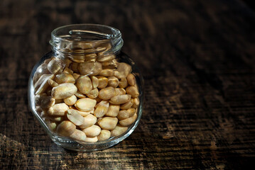Peanuts in a glass transparent jar. Nuts on an old shabby board. Jar on a brown wooden table close...