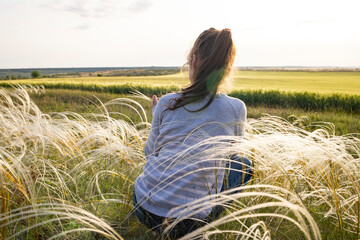 A little girl sits on the background of nature in a feather grass in the rays of the setting sun.