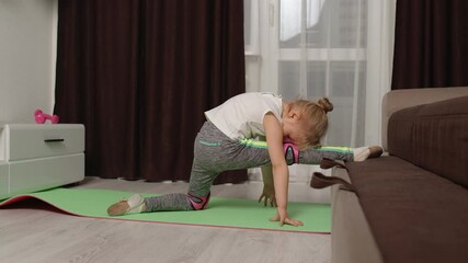 Fit little child kid training gymnastics fitness twine stretching workout on sofa. Healthy lifestyle, active leisure at home. Children girl in sportswear making sport exercises, warming up cardio