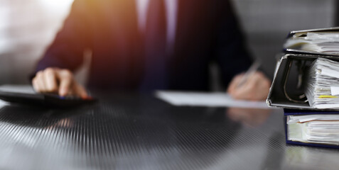 Binders with papers are waiting to be processed by unknown man accountant in blue blazer staying at home during covid pandemic. Taxes and audit concept