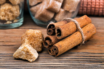 Cinnamon sticks with brown sugar pieces on a wooden background. Macro photography of spices.