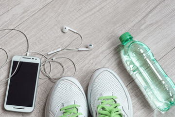 White sneakers, bottle of water, smartphone and headphones on the light wooden surface. Preparation for physical workout. Active healthy lifestyle concept.