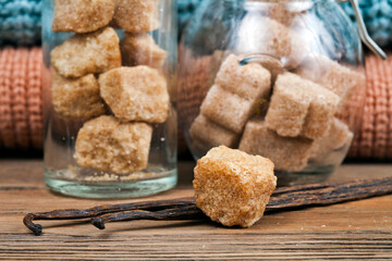 Vanilla beans with brown sugar pieces in the glass jars on a wooden background. Macro photography of spices.