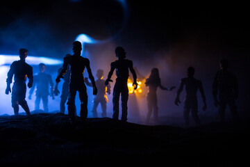 Fototapeta premium Scary view of zombies at cemetery dead tree, moon, church and spooky cloudy sky with fog, Horror Halloween concept with glowing pumpkin. Selective focus