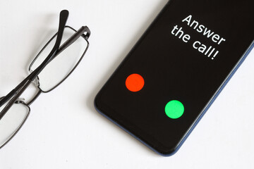 Black smartphone with an incoming call and the inscription: Answer the call lies on a white background next to the glasses. Calling parents. Caring for the elderly.