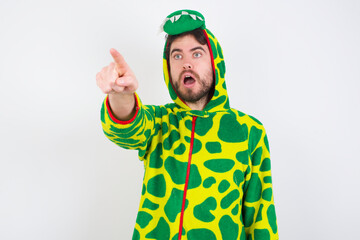 Young caucasian man wearing a pajama standing against white background Pointing with finger surprised ahead, open mouth amazed expression, something on the front.