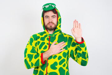 Young caucasian man wearing a pajama standing against white background Swearing with hand on chest...