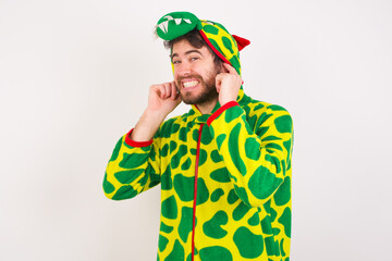 Young caucasian man wearing a pajama standing against white background covering ears with fingers with annoyed expression for the noise of loud music. Deaf concept.