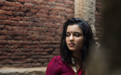 Portrait of beautiful Indian girl in heritage stepwell wearing traditional Indian red saree, gold jewellery and bangles holding religious plate. Maa Durga agomoni shoot concept