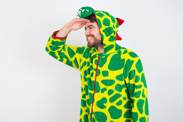 Young caucasian man wearing a pajama standing against white background very happy and smiling looking far away with hand over head. Searching concept.