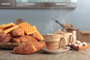 Breakfast with black coffee and fresh pastries on a kitchen table.