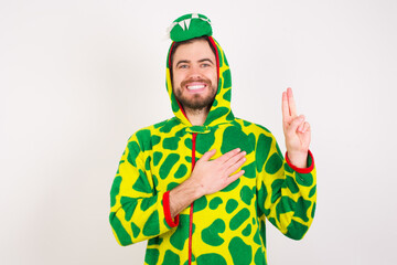 Young caucasian man wearing a pajama standing against white background smiling swearing with hand...