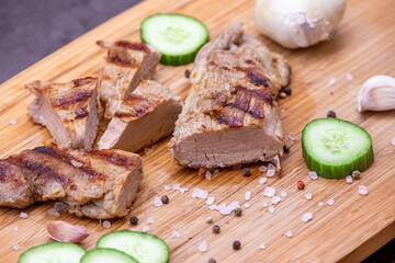 Grilled pork tenderloin cut on a wooden board. Grilled meat with cucumber, garlic and salt