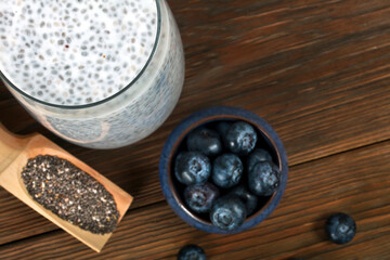 Chia pudding in a glass with blueberries and scoop of chia seeds on a wooden background. Healthy eating concept. Top view.