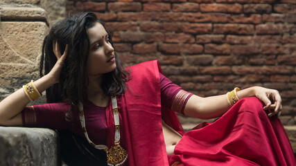 Portrait of beautiful Indian girl in heritage stepwell wearing traditional Indian red saree, gold...