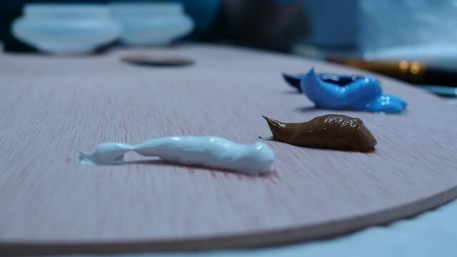 the girl's hand squeezes oil paints from the tube onto the palette.