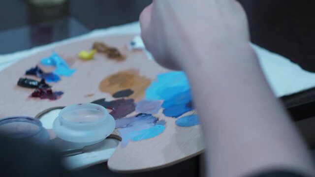the girl stirs the oil paints with a brush from the palette. close-up art palette.