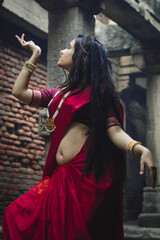 Portrait of beautiful Indian girl in heritage stepwell wearing traditional Indian red saree, gold...