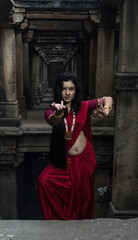 Portrait of beautiful Indian girl in heritage stepwell wearing traditional Indian red saree, gold...