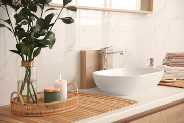 Fototapeta na wymiar Vase with beautiful branches, candles and fresh towels near vessel sink in bathroom. Interior design