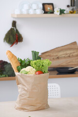 Paper bag full of vegetables on the table in kitchen interiors. Healthy meal and vegetarian concept