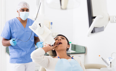 Dentist taking teeth radiography to hispanic female patient lying in chair in dentistry office