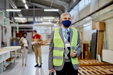 Quality control inspector wearing face mask while walking through woodworking industrial facility.