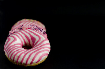 Donut with pink icing lies on a black background with copy space