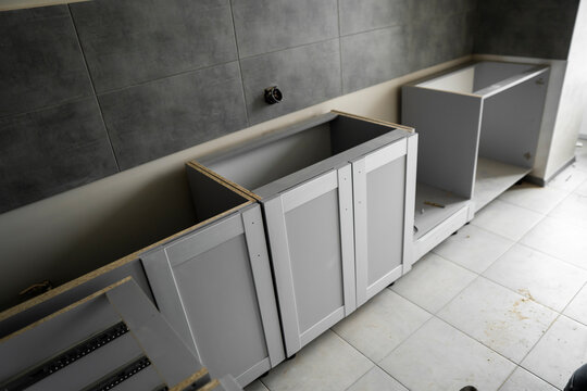 Lower custom kitchen cabinets installation with a furniture facades mdf. Gray modular kitchen from chipboard material on a various stages of installation. A frame furniture fronts mdf profile.