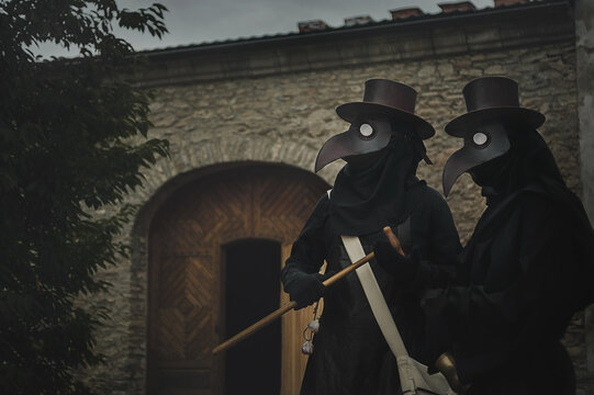 two plague doctors in masks on medieval castle background. Reconstruction of medicine costumes. Mascarade historical costumes and mask 