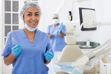 Portrait of smiling hispanic woman dentist preparing tools at modern dental office..