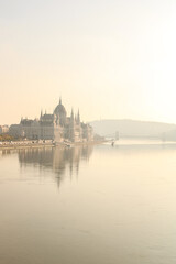Hungarian Parliament landscape in sunset light next to the Danube with boats with foggy air and Gellert hill in the background and the Chain bridge