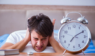 Man in bed frustrated suffering from insomnia with an alarm cloc