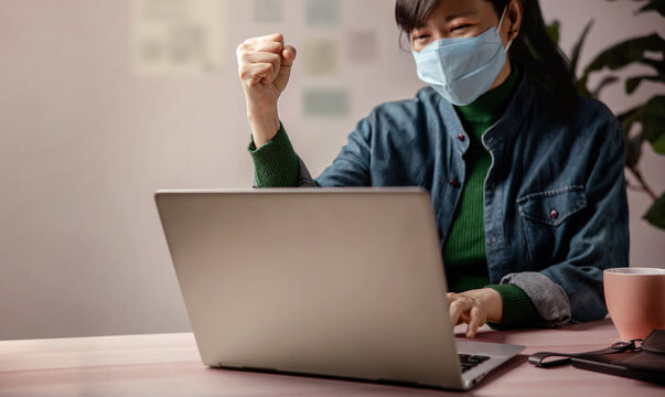 Small Business And Successful During Coronavirus Concept. Blurred Gladful Business Woman Wearing Mask, Working On Computer Laptop In Office. Focus On Hand. Business Achieves Goals. Celebrating Success