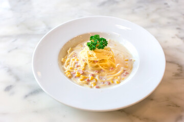 Spaghetti in white cream sauce mixed with ham and corn and served on a white plate in Italian food restaurant.