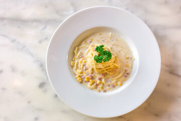 Spaghetti with ham and corn cream sauce put on a white plate on marble table as a background.