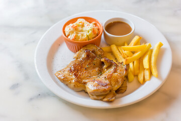 Chicken steak marinated black pepper in Thai style food served with French fried, coleslaw and blown sauce put on a white plate.
