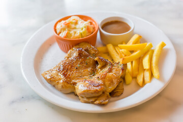 Chicken steak marinated black pepper in Thai style food served with French fried, coleslaw and blown sauce put on a white plate.