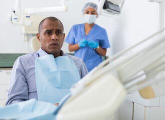 Obraz premium Portrait of scared Latin American sitting on dental chair waiting for treatment procedures in dentist office