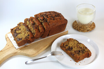 Sliced banana bread loaf on wooden board, a slice of banana bread on a plate, and a glass of milk