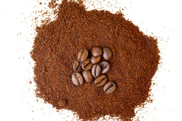 Roasted coffee beans at the top of a pile of ground coffee on an isolated white background.