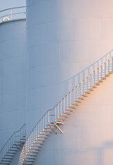 Morning sunshine on curve spiral staircase surface of white storage fuel tanks in vertical frame