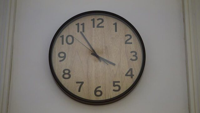 Total view of a ticking wall clock in wooden style with black digits, black clockhands and a black frame in 4K.
