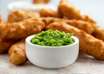 Battered Haddock fish, mini fingers with mashed peas, tartar sauce on white wooden board