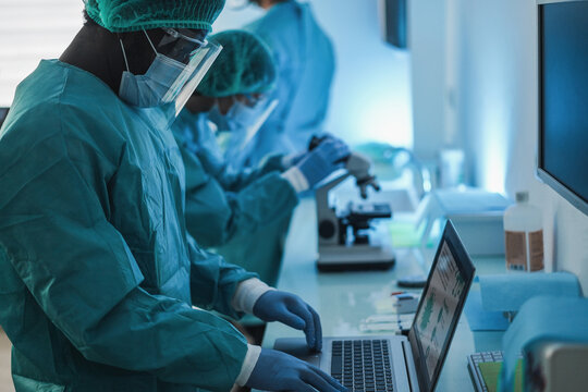 Medical Workers In Hazmat Suit Working With Computer And Micoroscope Inside Laboratory Hospital During Coronavirus Outbreak Wearing Safety Masks - Covid-19 Analysis Concept - Focus On African Man Face