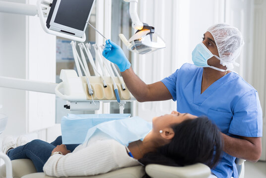 Qualified hispanic dentist pointing at teeth x-ray image on computer monitor explaining future treatment to female patient in dental clinic